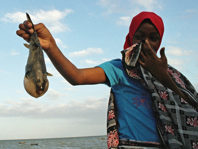 Mladá muslimka z vesnice Bagamoyo ukazuje rybu, kterou rybáři nechali ležet na pláži, protože není k jídlu