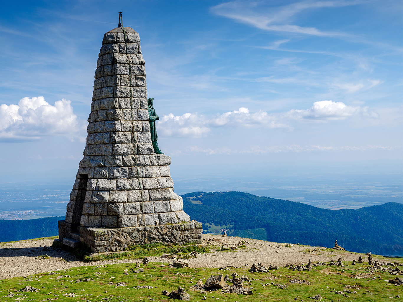Mohyla shlížející na zalesněné zaoblené vršky pohoří Vogézy