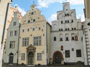 Tři různě barevné domy třech různých architektonických stylů v centru Rigy